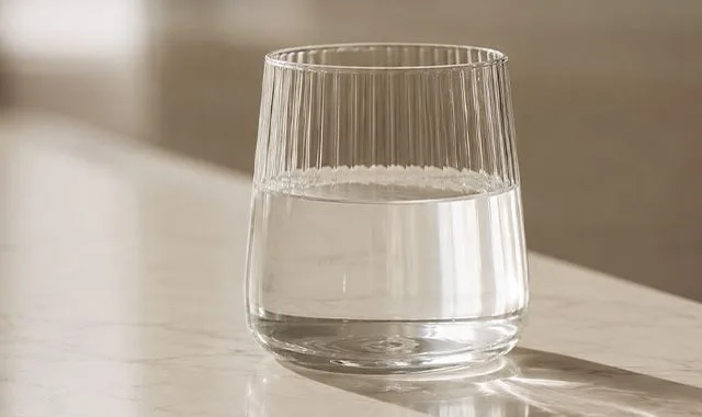 Ein geripptes Glas klares Kangen Water® auf einer sonnenbeschienenen Arbeitsfläche