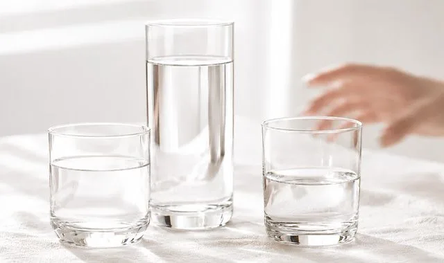 Drei Gläser frisches Wasser in verschiedenen Größen auf einem hellen Tisch